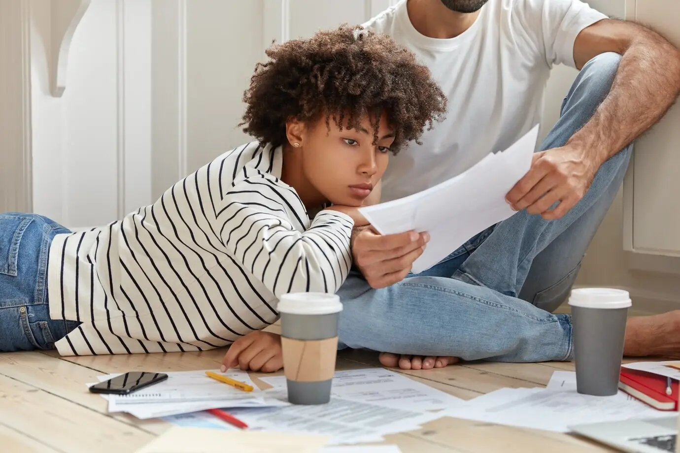 Женщина и мужчина-менеджеры позируют на полу, обсуждают отчет, узнают результаты продаж из бумаг, встречаются в домашней атмосфере, пьют кофе из одноразового стаканчика и анализируют прибыль компании. Концепция сотрудничества.