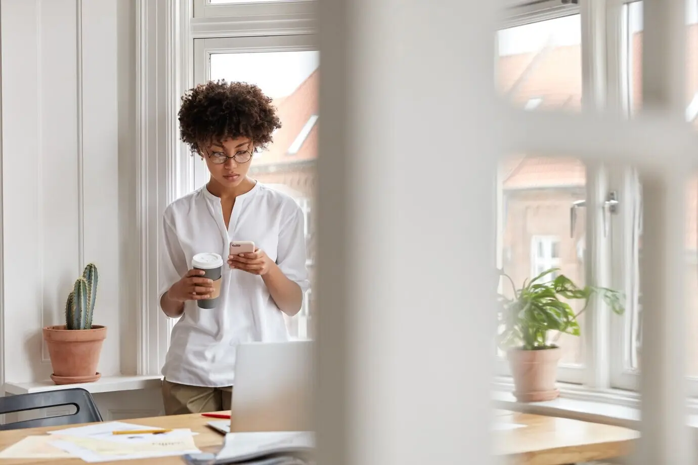 Занятая чернокожая успешная бизнес-леди или предпринимательница проверяет уведомление на мобильном телефоне и пьет кофе навынос.